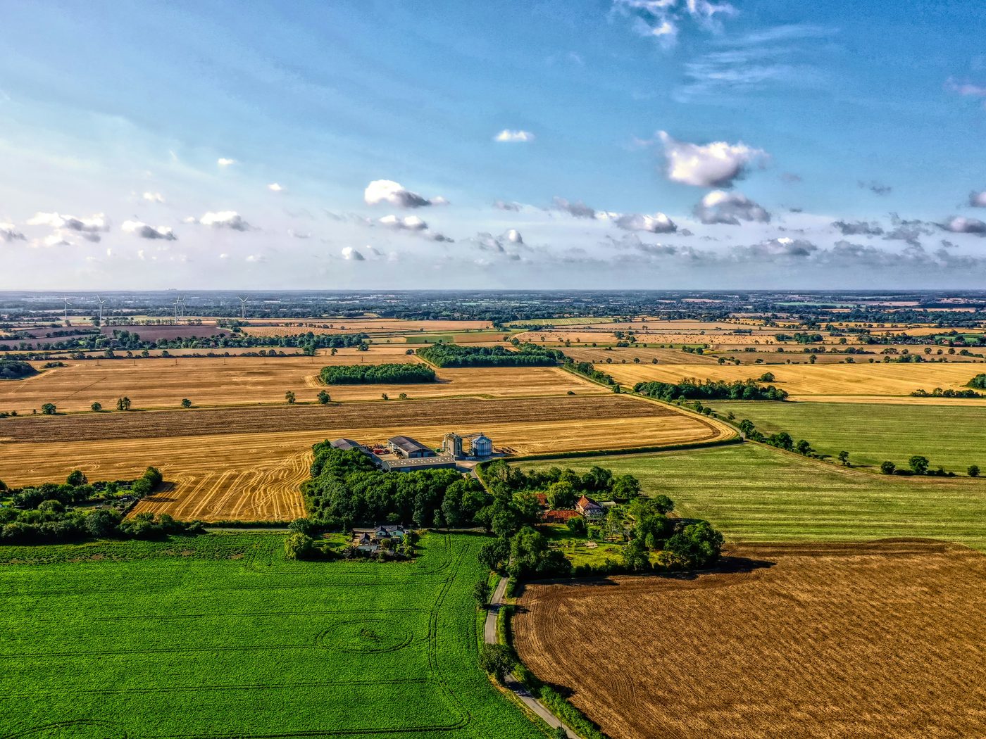 Aerial view of East Anglian arable farmland, with a working farm and grain stores among hedgerowed fields and wind turbines on the horizon